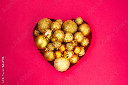 Christmas creative minimalism. Gold glitter. Christmas balls of different sizes are collected in a heart-shaped box on a pink background. Flat lay, top view. photo