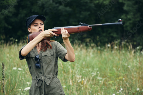 Woman on outdoor a woman holds a gun in front of her aiming at a hunt green leaves green 