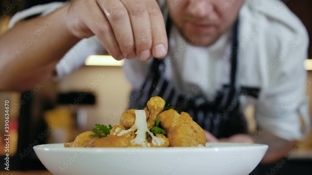 Close-up Professional Chef at Restaurant Kitchen Serves Dish Adding Final Ingredient by Hand. Cooking Vegetarian Food at Modern Home Cuisine. Delicious European Food. Preparing Meal on Kitchen Slow mo
