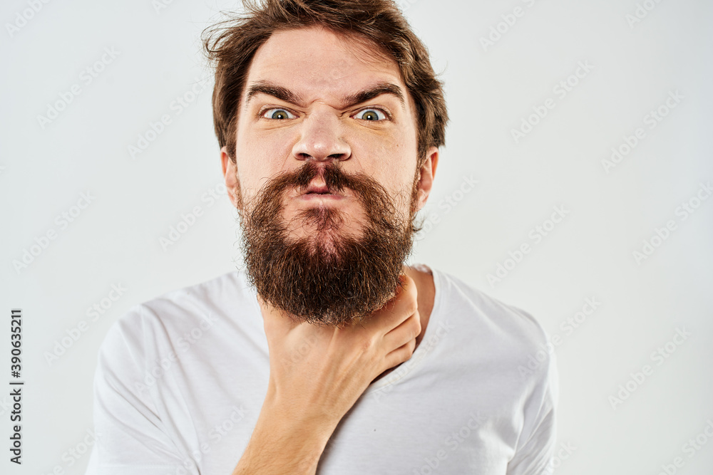 Emotional bearded man in a white t-shirt gestures with his hands light background