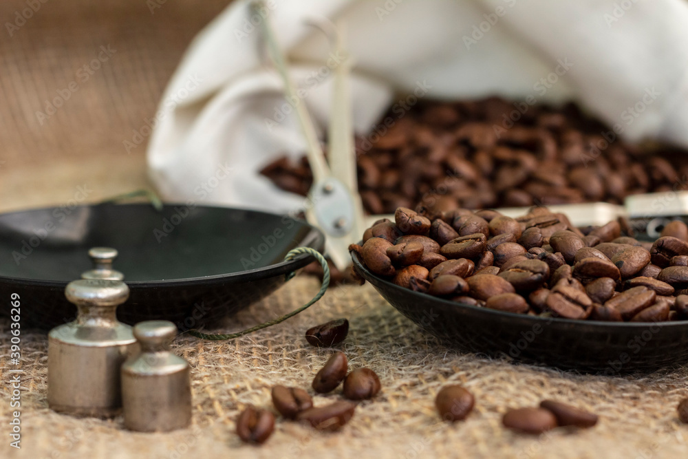 Roasted coffee beans, weighed on an antique hand scale with weights, lying on a table covered with burlap.
