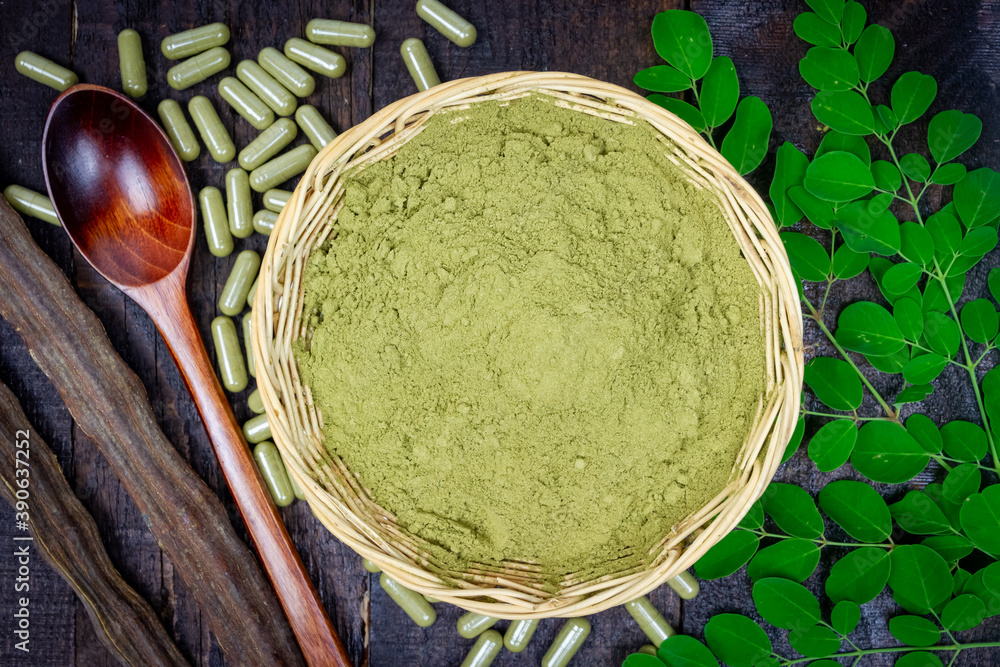 Close-up Moringa powder in wicker basket, Moringa fresh green leaves, pods, wooden spoon and capsules on wooden background. Close-up Moringa powder in wicker basket, Moringa fresh green leaves, pods, wooden spoon and capsules on wooden background.