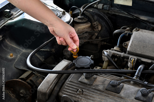 A woman checks the engine oil in an old car parked in the garage before leaving, wiping the car before traveling.