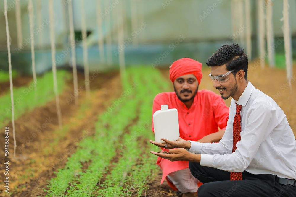 Young indian agronomist and farmer showing bottle at greenhouse Young indian agronomist and farmer showing bottle at greenhouse
