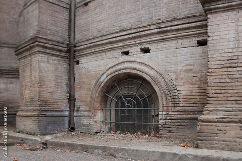 The arch window in the brick wall of a cathedral with rusty metallic grid on it. Architectural detail.