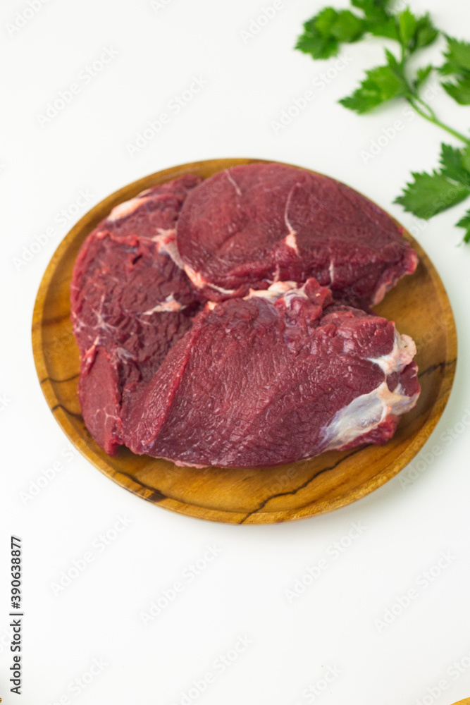 Close of view of slices fresh beef on wooden brown plate, with green celery and spring onion. White isolated background. Close of view of slices fresh beef on wooden brown plate, with green celery and spring onion. White isolated background.