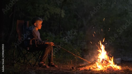 Child boy sitting near capming fire with bright sparks at night. photo