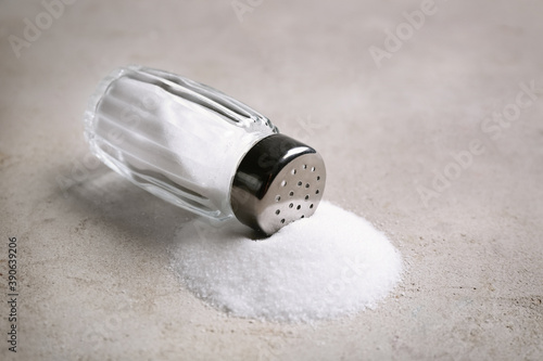 Scattered salt and shaker on light grey table, closeup