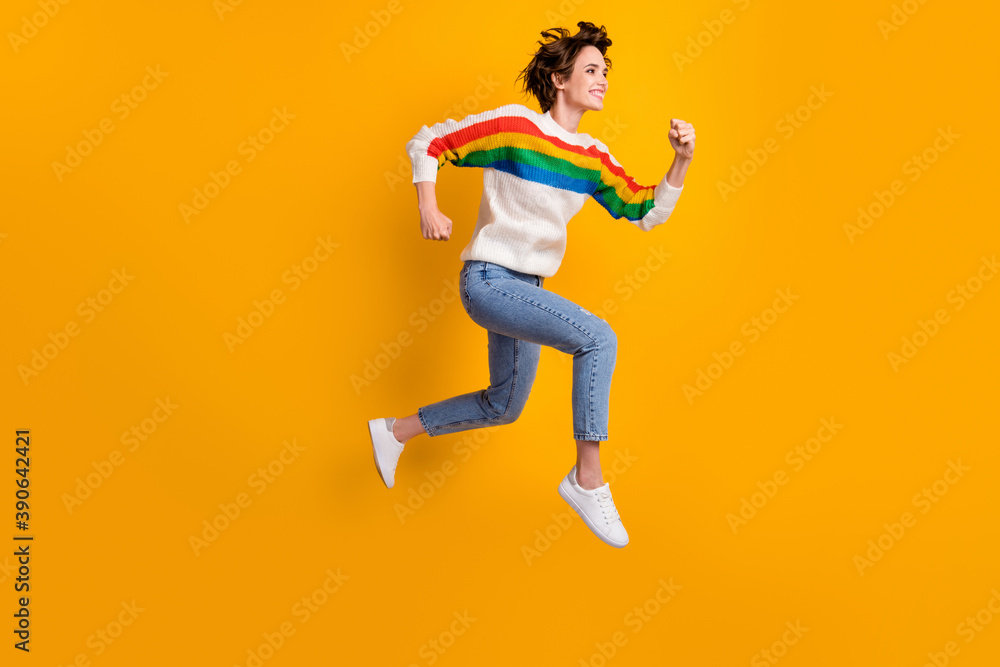 Profile full size photo of positive cool girl run in air wear rainbow sweater denim jeans white sneakers isolated on yellow background