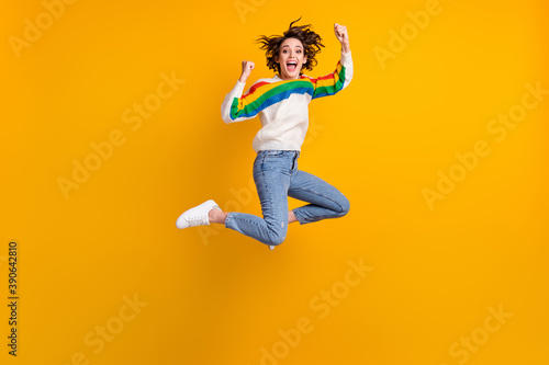 Profile full size photo of hooray funny young woman jump wear rainbow sweater denim jeans white footwear isolated on yellow background