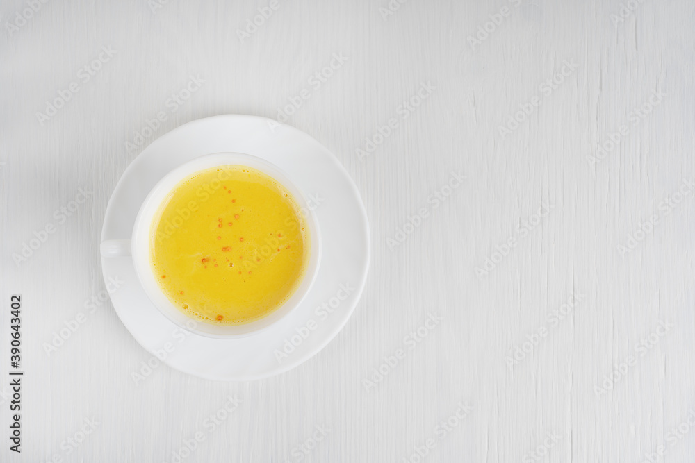 Top view of single cup of golden or turmeric milk which is Indian homemade popular drink used as alternative remedy to boost immunity served on plate on white wooden background. Image with copy space Top view of single cup of golden or turmeric milk which is Indian homemade popular drink used as alternative remedy to boost immunity served on plate on white wooden background. Image with copy space