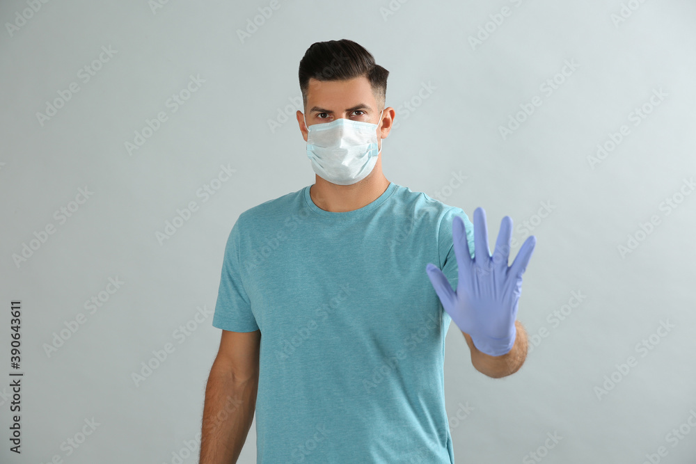Man in protective face mask and medical gloves showing stop gesture on grey background Man in protective face mask and medical gloves showing stop gesture on grey background
