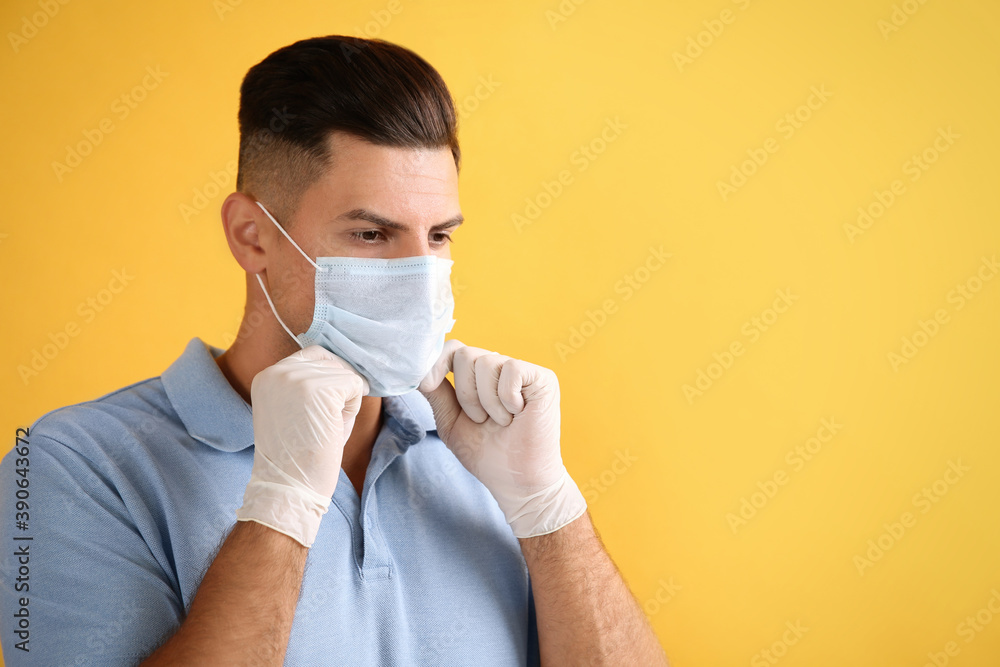 Man in medical gloves putting on protective face mask against yellow background. Space for text