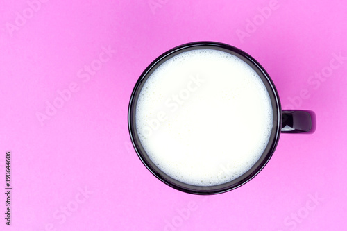Top view of milk in black ceramic cup on pink background with copy space. 