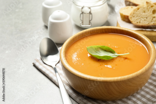 Tasty creamy pumpkin soup with basil in bowl on grey table