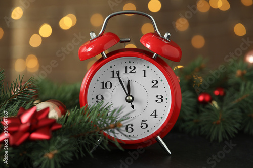 Alarm clock with decor on black table against blurred Christmas lights, closeup. New Year countdown