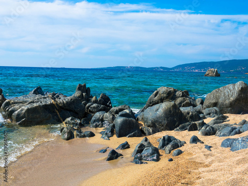 Panoramic view of waves washing onto rocks and sand at Liamone beach under a blue sky photo