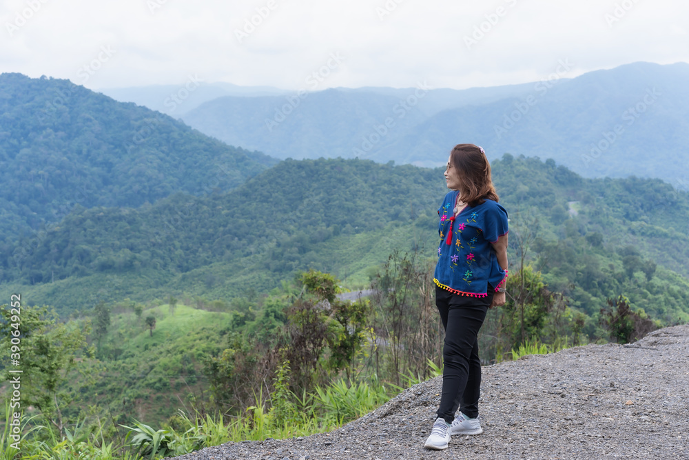 Adult traveling woman wearing sunglasses standing and smiling on the top of the mountain cliff with relaxing mood and watching beautiful view of woods and clouds foggy on vacation. Nature background Adult traveling woman wearing sunglasses standing and smiling on the top of the mountain cliff with relaxing mood and watching beautiful view of woods and clouds foggy on vacation. Nature background