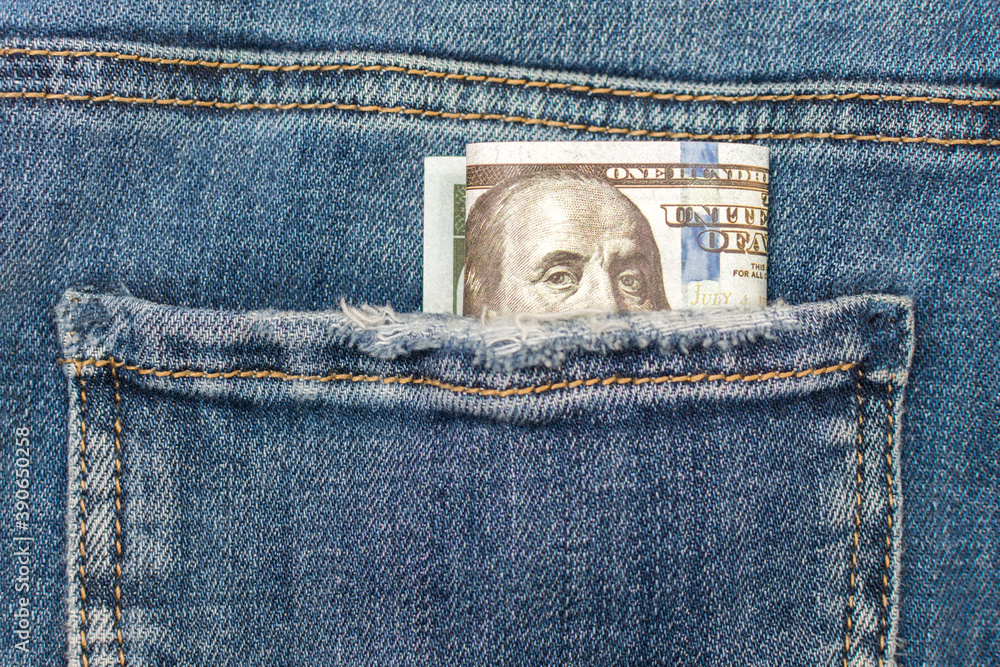 a 100 dollar bill peeps out of his jeans pocket. Close-up, horizontal photo. Concept - a stash for a rainy day, pocket money. a 100 dollar bill peeps out of his jeans pocket. Close-up, horizontal photo. Concept - a stash for a rainy day, pocket money.