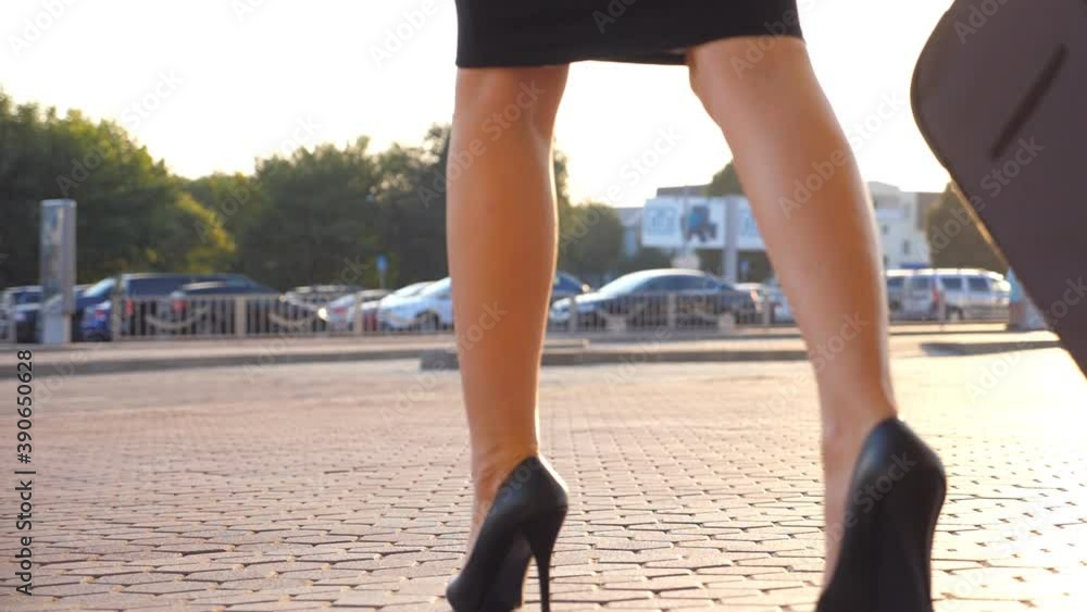 Business woman walking with her suitcase from airport hall or waiting room. Young girl in heels going from terminal and rolling luggage on wheels. Business lady stepping at city street. Slow motion Business woman walking with her suitcase from airport hall or waiting room. Young girl in heels going from terminal and rolling luggage on wheels. Business lady stepping at city street. Slow motion
