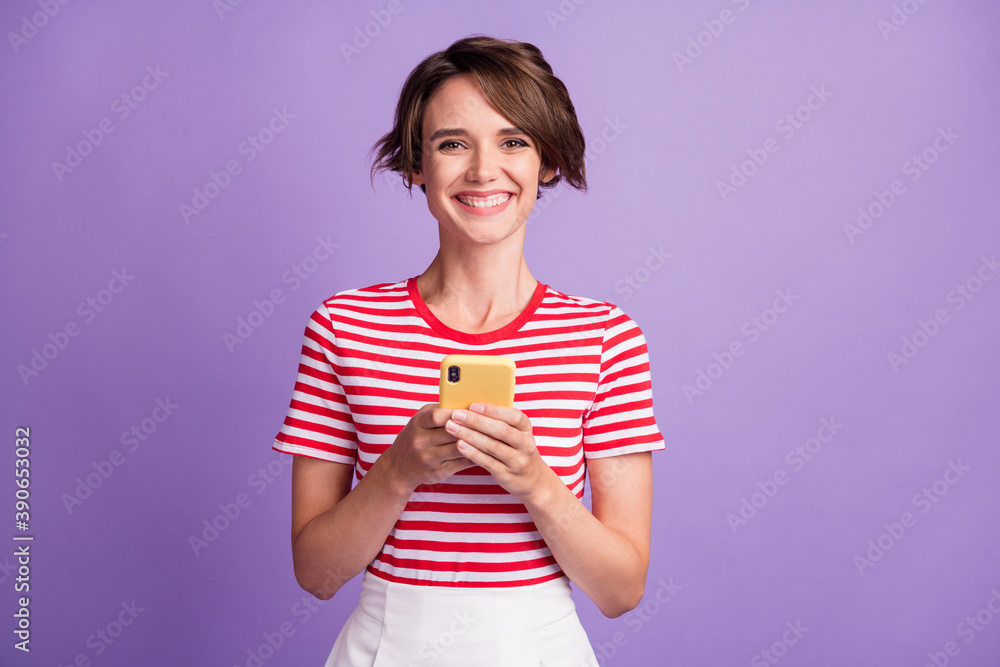 Photo of cheerful pretty lady hold telephone look camera white smile wear striped t-shirt isolated purple color background Photo of cheerful pretty lady hold telephone look camera white smile wear striped t-shirt isolated purple color background