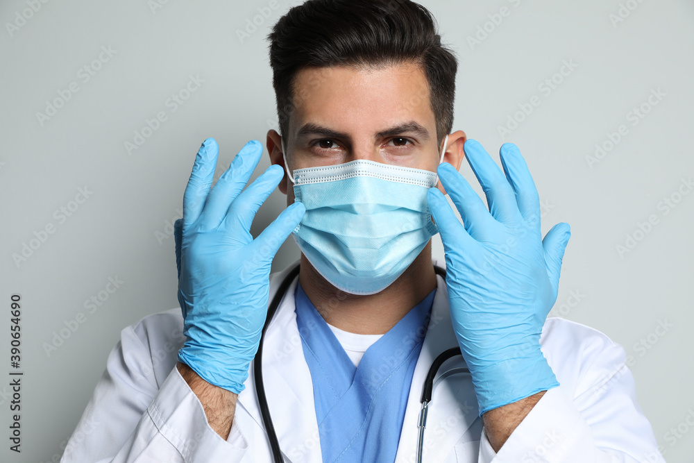 Doctor in protective mask and medical gloves against light grey background