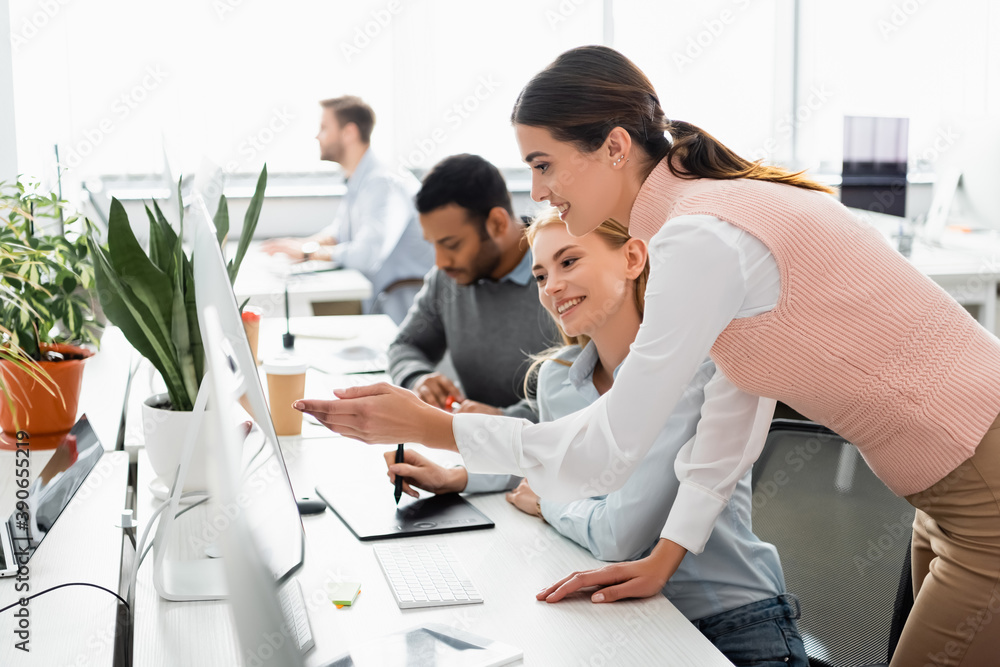 Smiling businesswomen using graphics tablet and computer in office Smiling businesswomen using graphics tablet and computer in office