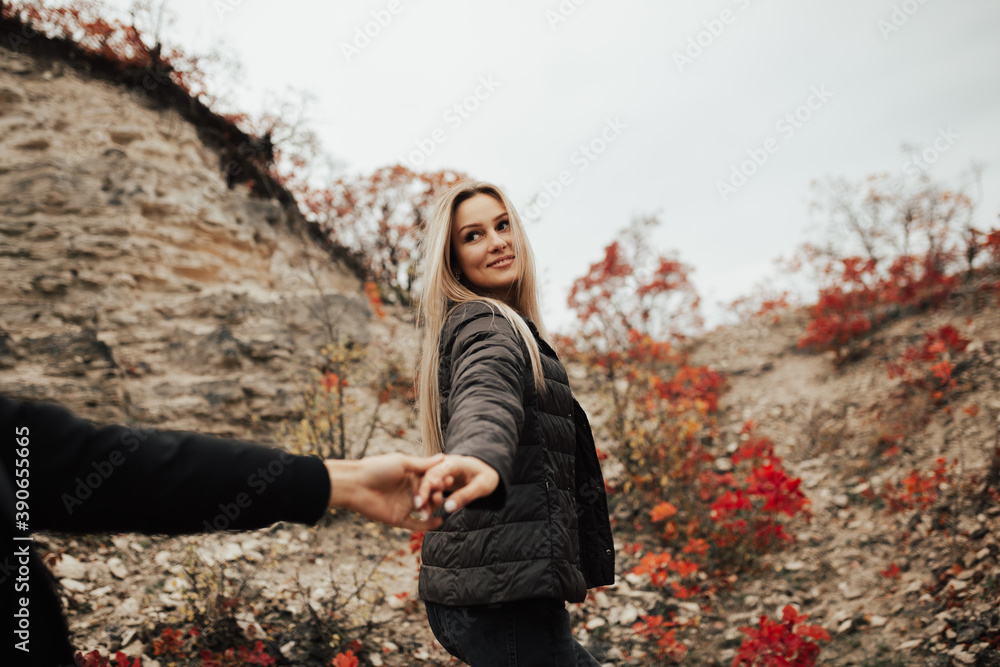 Smiling girl pulling man's hand on the rocky mountain. Follow me.
