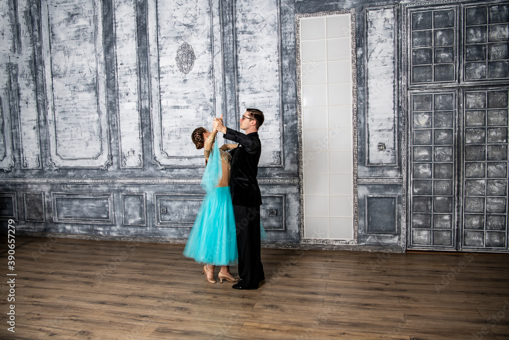 a young man in a black suit is dancing with a girl in a turquoise dress in the dance hall a young man in a black suit is dancing with a girl in a turquoise dress in the dance hall