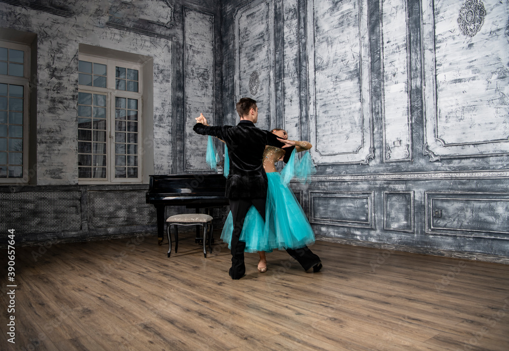 a young man in a black suit is dancing with a girl in a turquoise dress in the dance hall