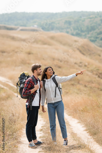 African american woman pointing with finger near smiling boyfriend with backpack on path outdoors © LIGHTFIELD STUDIOS