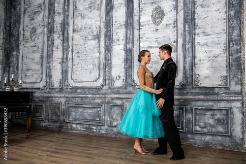 a young man in a black suit is dancing with a girl in a turquoise dress in the dance hall