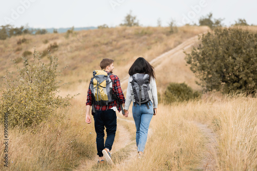 Back view of hikers with backpacks and smartphone holding hands while walking on path