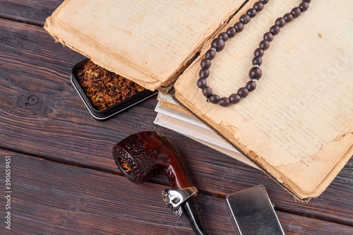 Top view vintage accessoires. Very old book with bead necklace. smoking pipe and lighter on rustic wooden table. photo