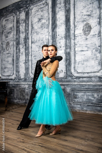 a young man in a black suit is dancing with a girl in a turquoise dress in the dance hall © константин константи