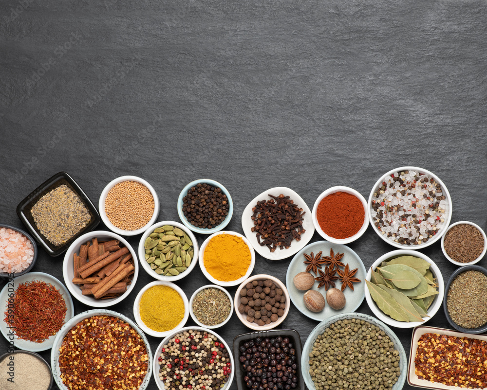 Assortment of aromatic spices and herbs in small bowls on black stone background with copy space