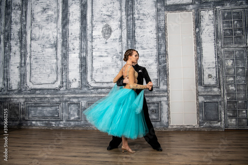 a young man in a black suit is dancing with a girl in a turquoise dress in the dance hall