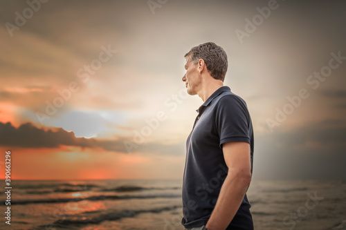 man standing at the beach looking into the distance with dramatic sky