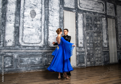 young man dancing with a girl in a blue ballroom dress in a gray dance hall