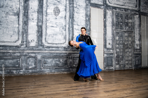 young man dancing with a girl in a blue ballroom dress in a gray dance hall © константин константи