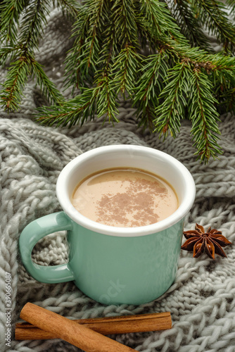 mug of cocoa with cinnamon on a knitted blanket with Christmas tree branches.