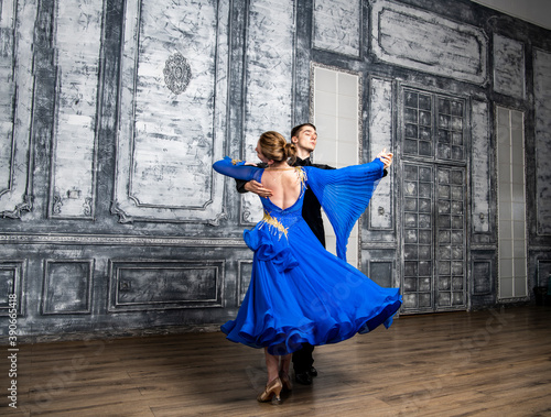 young man dancing with a girl in a blue ballroom dress in a gray dance hall