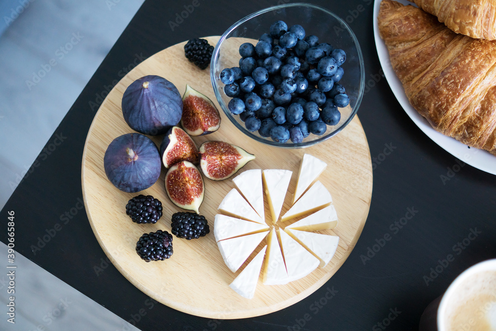 Camembert cheese, figs, blueberries and blackberries on a wooden round Board, coffee and croissants. Breakfast on the table Camembert cheese, figs, blueberries and blackberries on a wooden round Board, coffee and croissants. Breakfast on the table