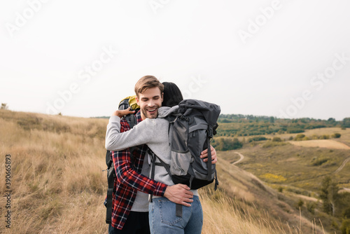 Smiling traveler with backpack embracing African American woman during trip
