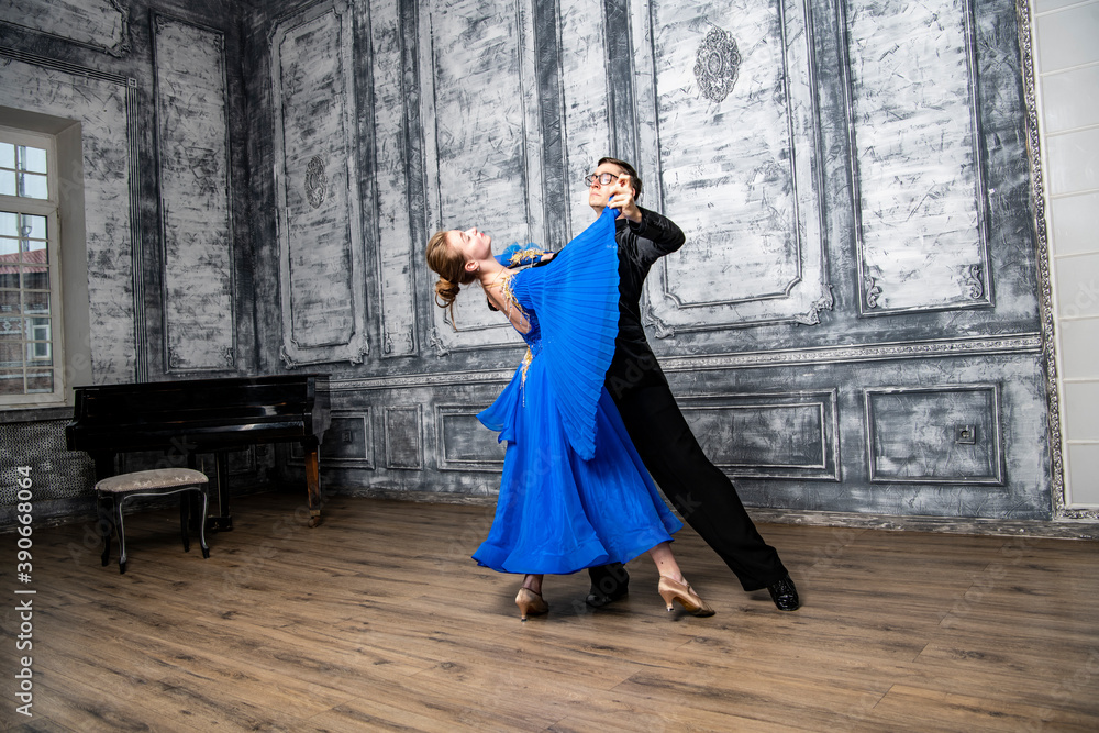 Naklejka premium young man dancing with a girl in a blue ballroom dress in a gray dance hall