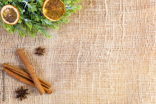 close-up of cinnamon stick, anise, green wreath with lights and dry oranges, bright natural and vintage christmas decoration on jute background, raw ingredients, flat lay