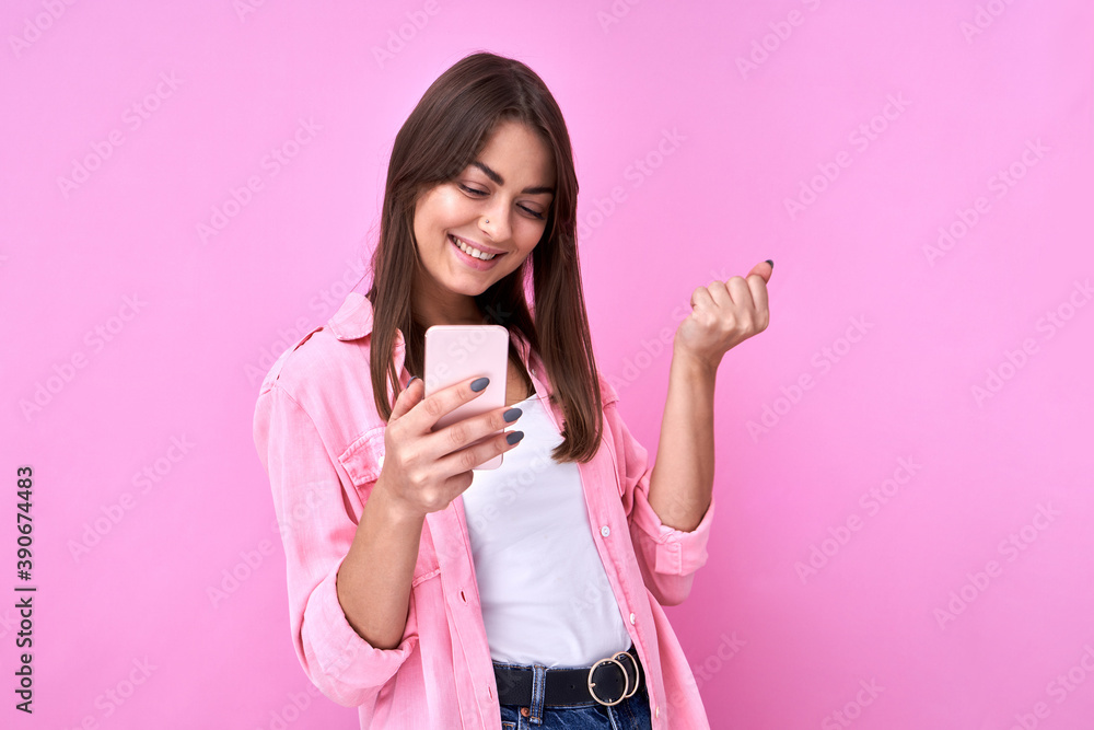 Brunette attractive girl holds mobile phone in her hand and rejoices at the good news, clenches her fists isolated in pink studio with copy space Brunette attractive girl holds mobile phone in her hand and rejoices at the good news, clenches her fists isolated in pink studio with copy space