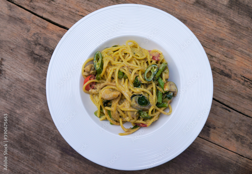 Top view Green curry spaghetti with chicken in a white plate placed on a wooden table. Top view Green curry spaghetti with chicken in a white plate placed on a wooden table.