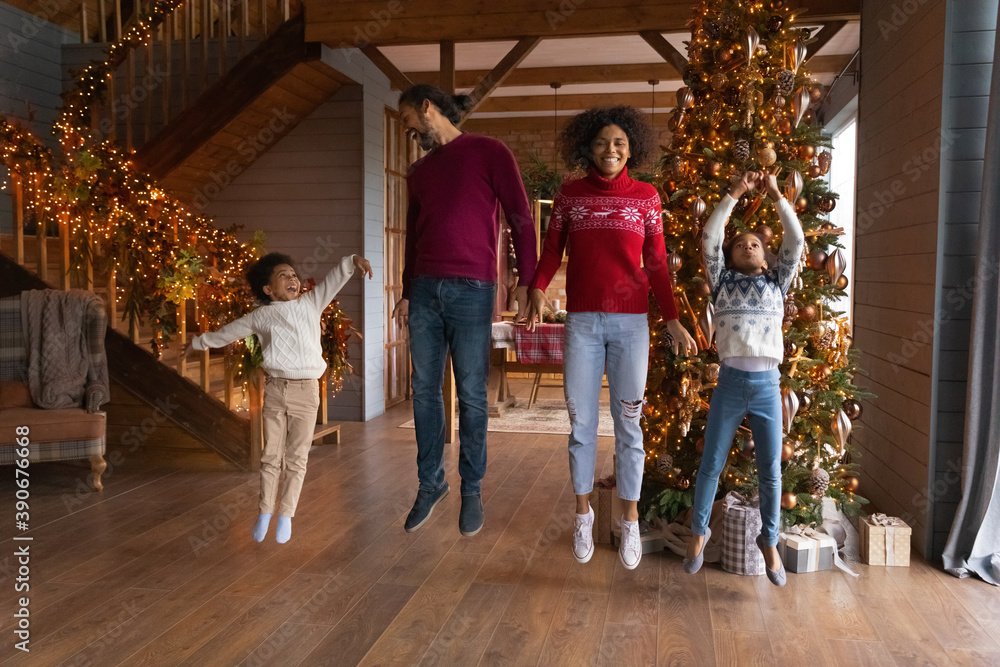 Overjoyed African American family jumping near Christmas tree, enjoying winter holidays at home, happy mother and father with son and daughter having fun, laughing and dancing, flying in air