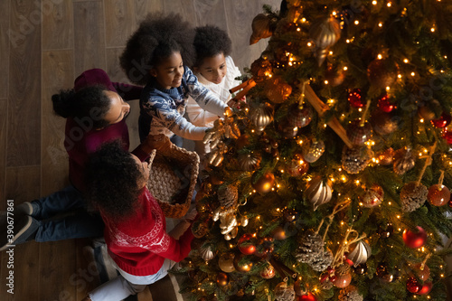 Top view African American family with two adorable children decorating Christmas tree at home, happy mother and father with little son and daughter wearing sweaters spending winter holidays together